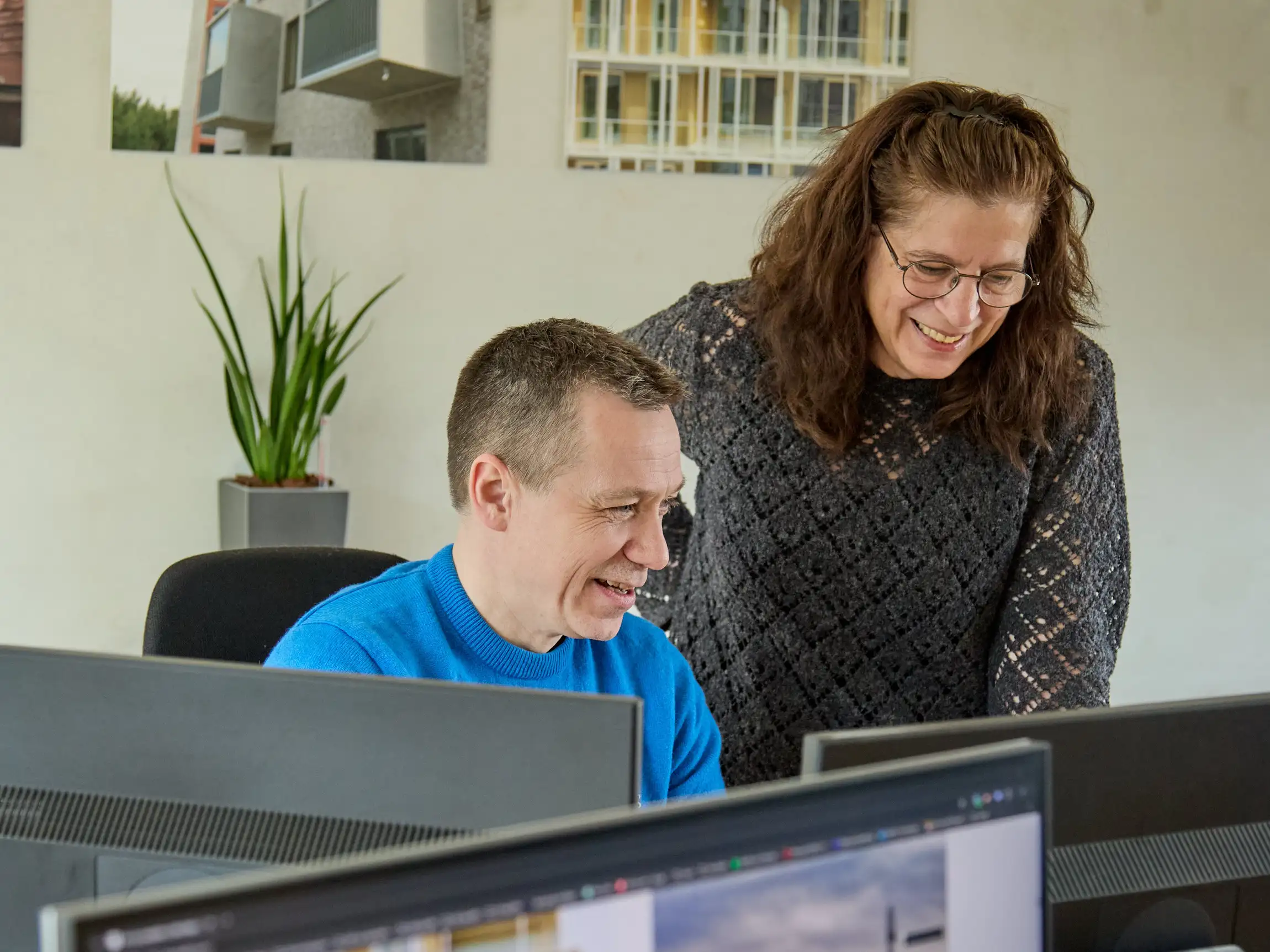 Twee kantoormedewerkers lachen terwijl ze samenwerken